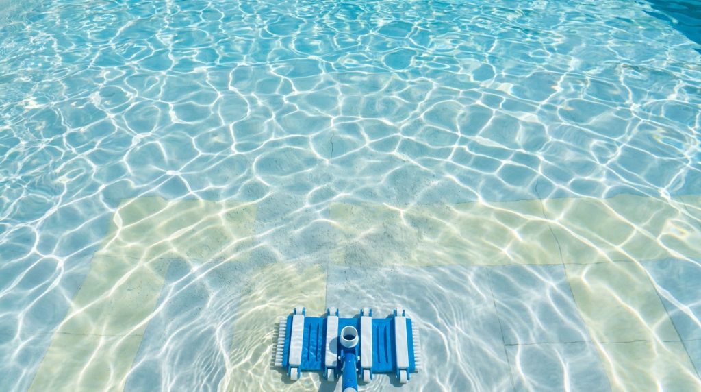 Brosse de balai aspirateur de piscine immergée au fond d'un bassin à l'eau claire avec des reflets.